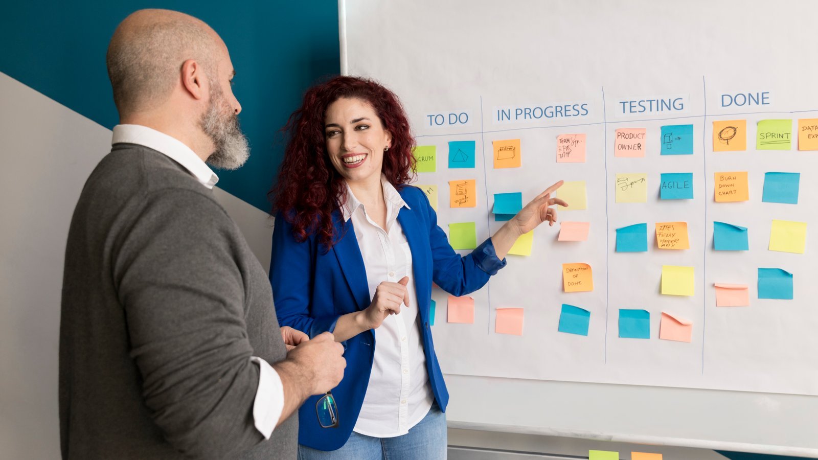 Two colleagues discussing a sprint board of sticky notes across to-do, in progress, testing and done columns